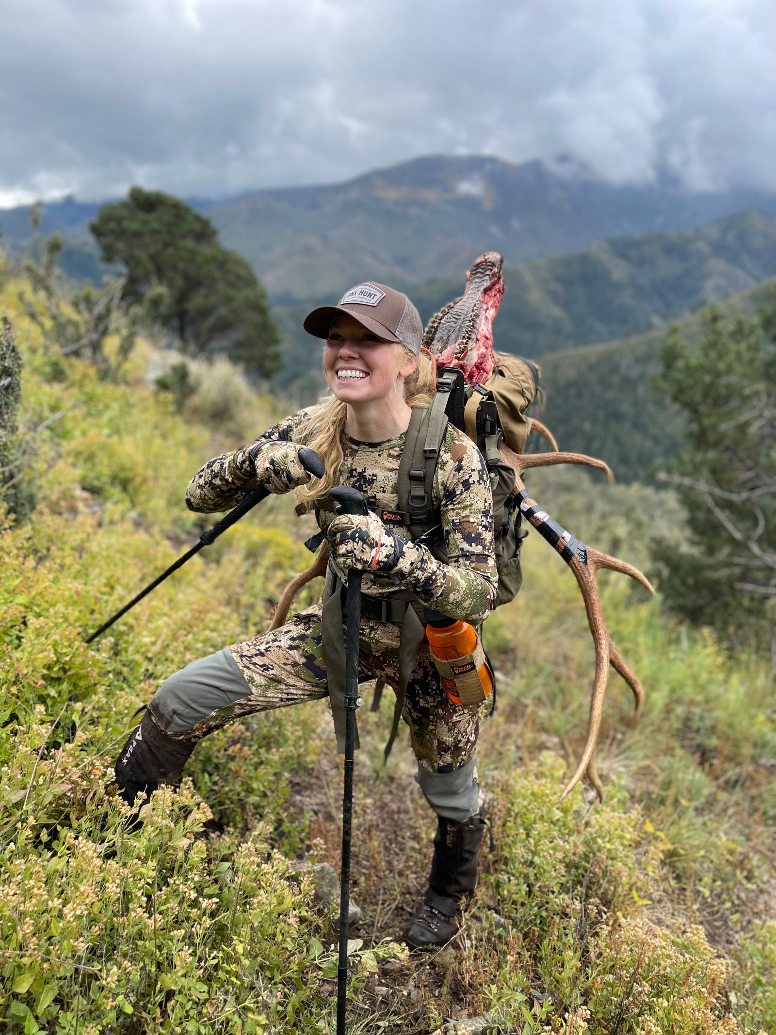 A female hunter standing on the mountainside with a bull elk 