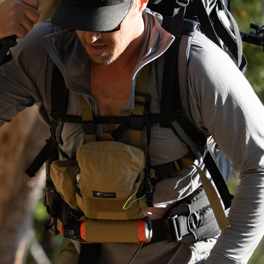 A backpacker hiking up a trail and breathing heavily while wearing the Stone Glacier Synthetic Hoody in stone grey with zipper fully open.