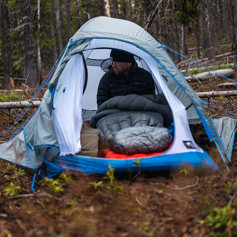 A backcountry hunter partially positioned within his sleeping bag as viewed through the front door of the Stone Glacier Sky Solus 1P Tent.